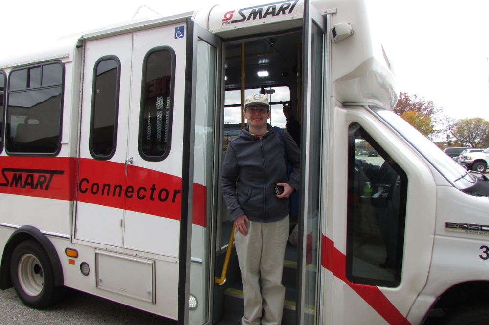 A side view of the smart transportation bus with a happy student standing on its steps.